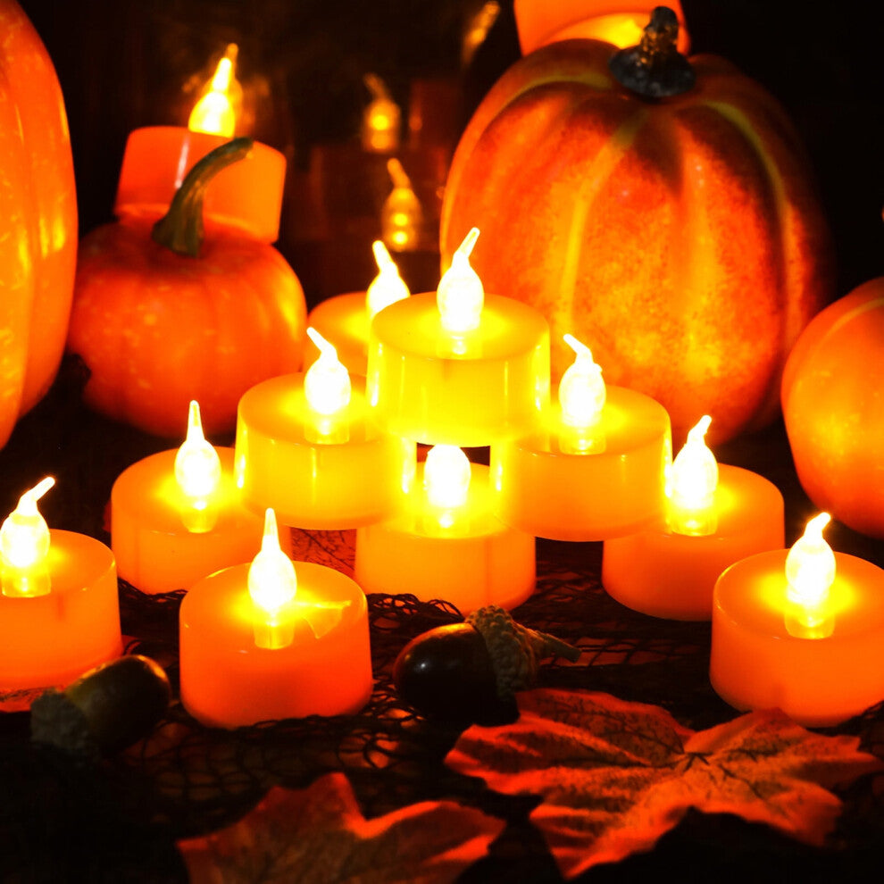 A 24-pack of orange LED flameless flickering tea light candles glowing warmly on a dark table decorated for Halloween.