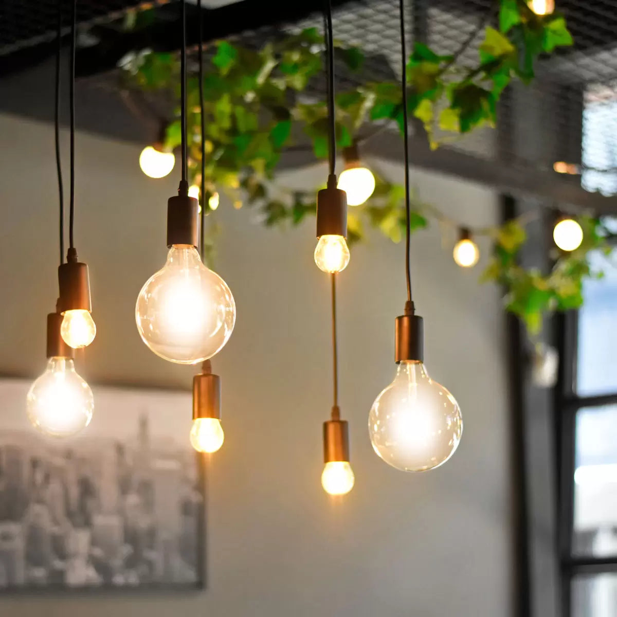 A pair of 4lite WiZ Connected E27 Amber Filament Smart Bulbs glowing with a warm orange vintage light inside a contemporary living room setting.