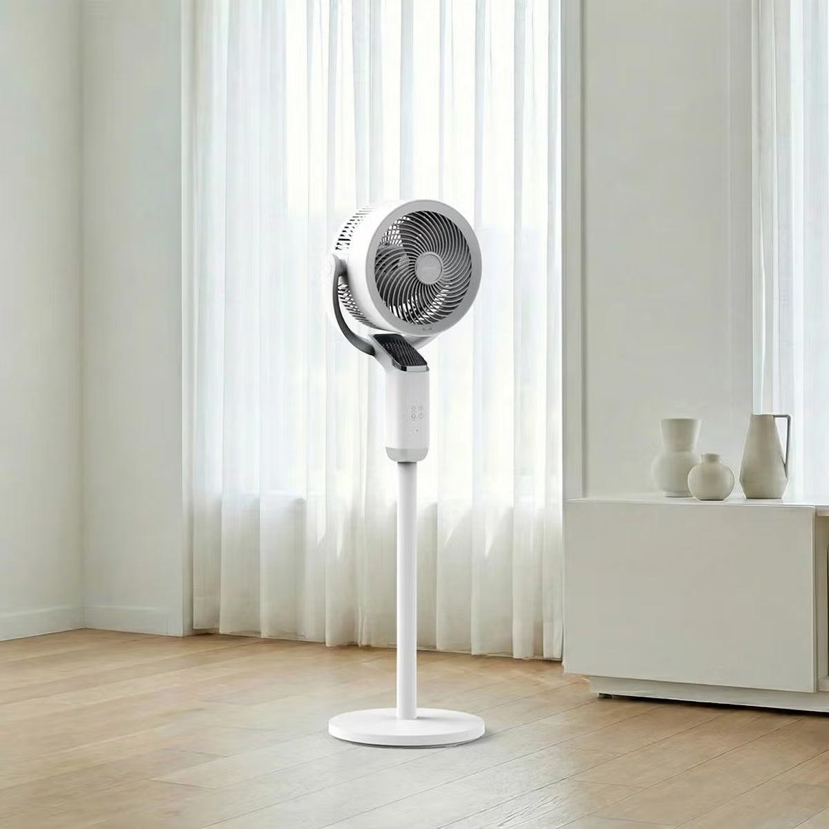 Modern white Airmate FA20-RD239 pedestal fan featuring a sleek slanted smart display screen, vertical support pole, and round base set in a sunlit living room.