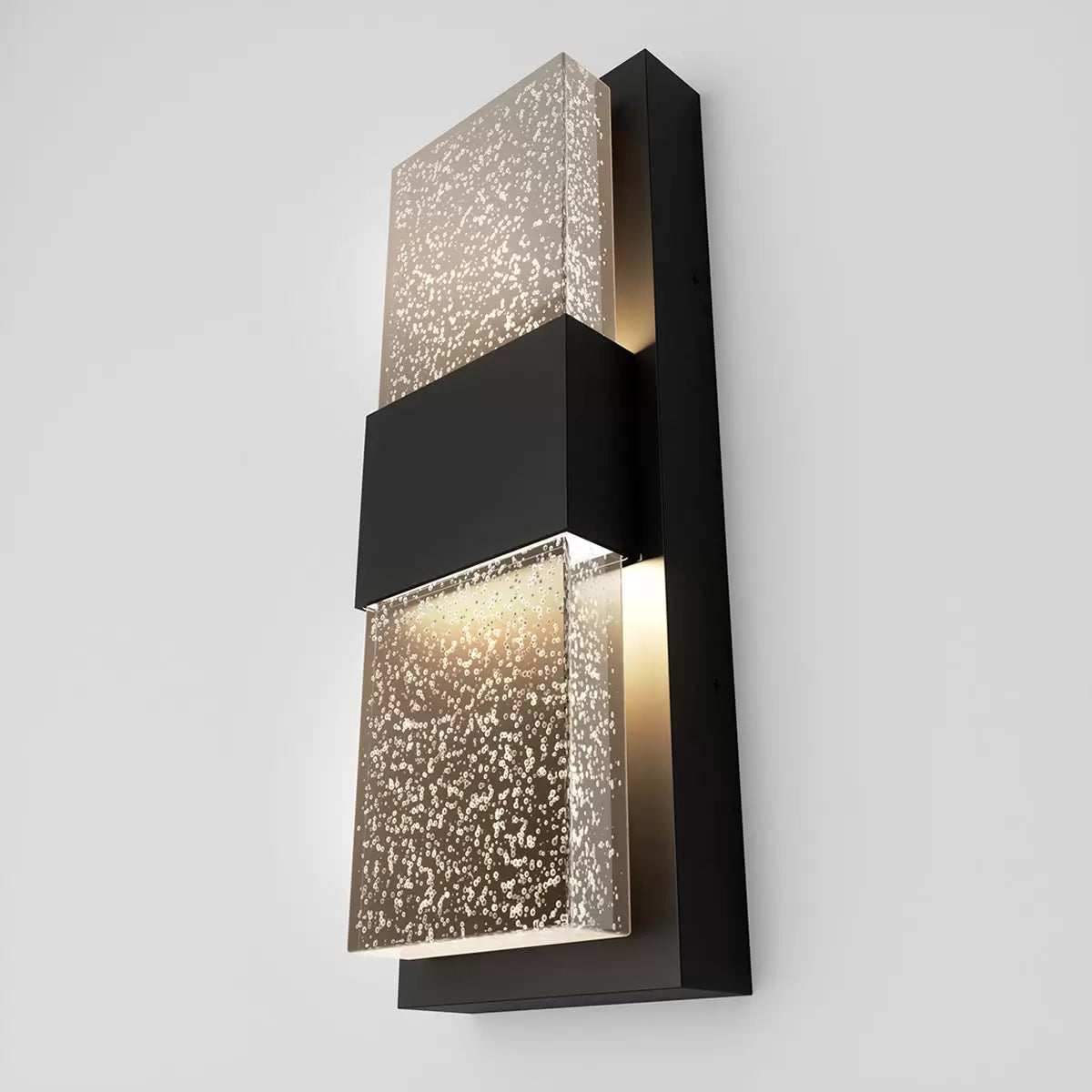 Artika Mazza Bubble wall sconce in matte black mounted on an exterior wall, showing the textured bubbled glass emitting a warm golden glow.