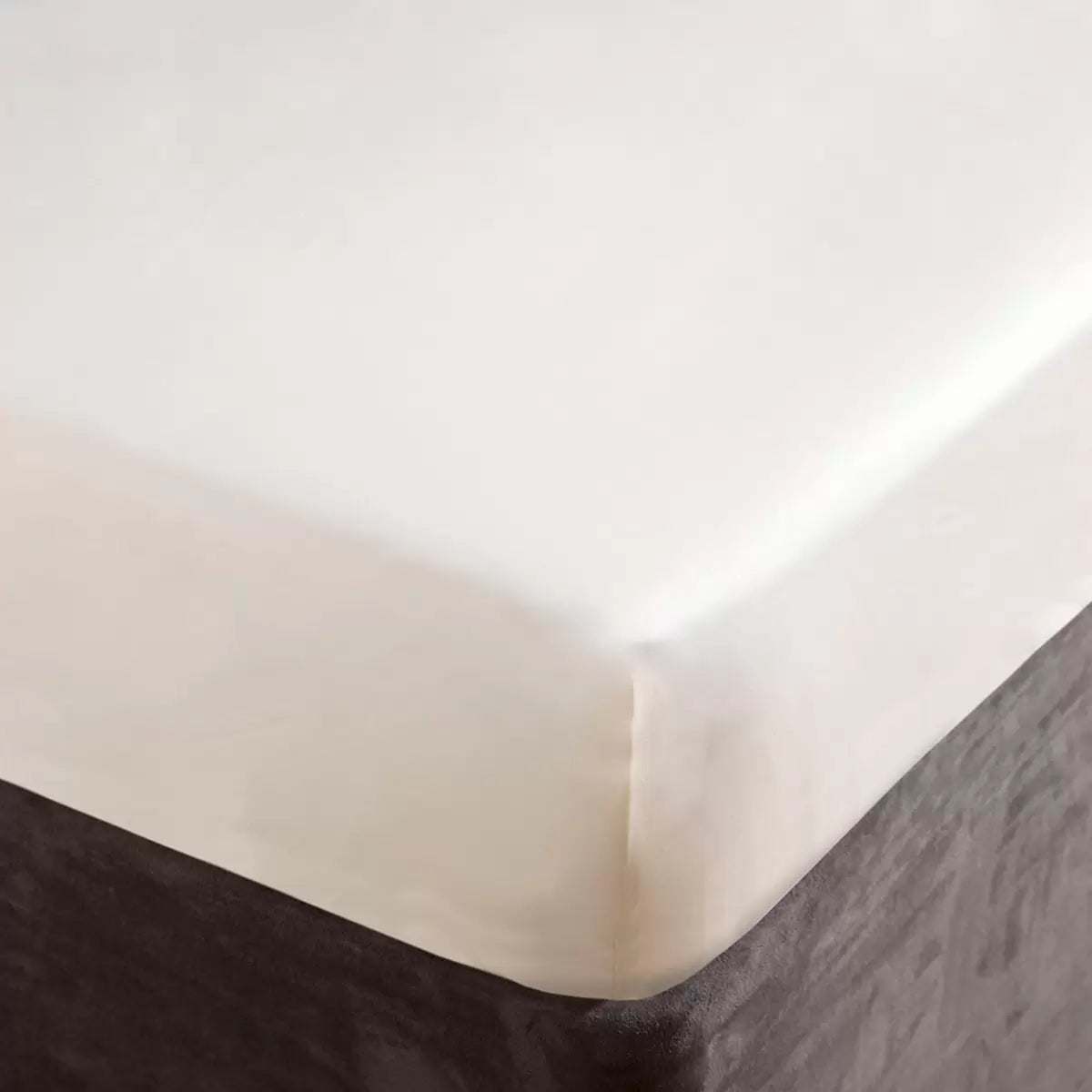A close-up view of the smooth, lustrous surface of the Belledorm 1000 thread count ivory Egyptian cotton sateen fitted sheet showing its tight weave and neat corner stitching on a neatly made bed.