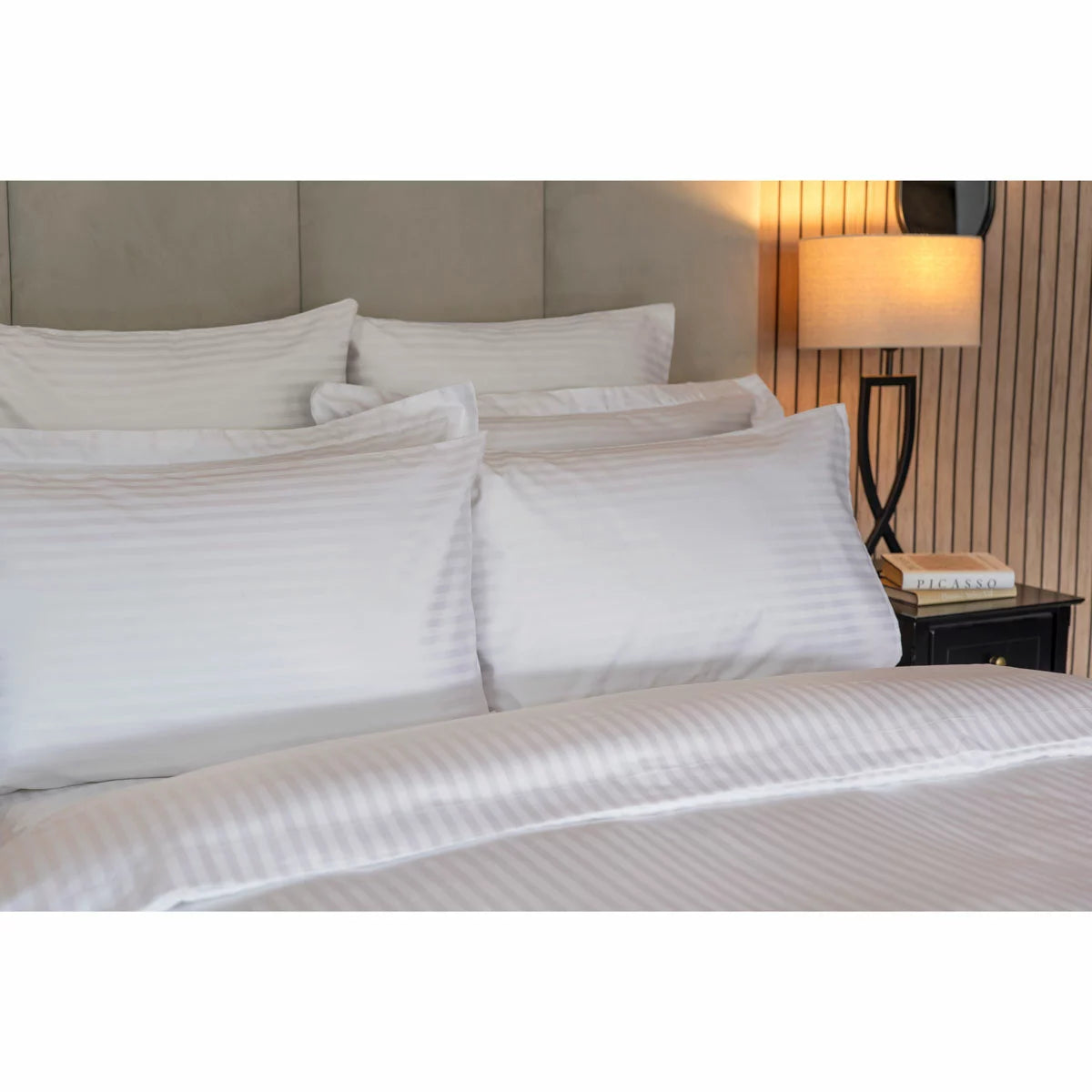 Neat arrangement of the Belledorm 540 thread count white satin stripe duvet cover set with matching pillowcases folded on a minimalist wooden bed frame.