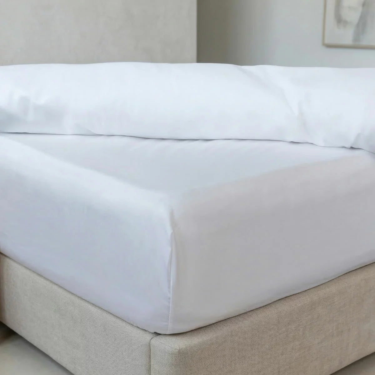 Close-up view of the crisp white Belledorm bamboo-cotton fitted sheet stretched tightly over the corner of a thick single mattress in a bright bedroom.