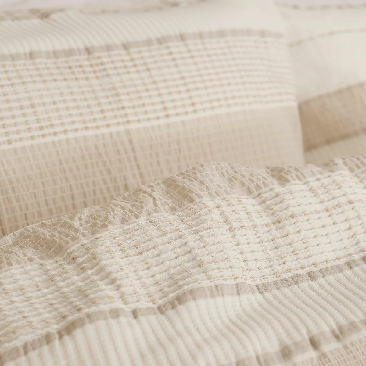 A close-up shot of the Belledorm Rahil natural bedding set showing the contrast between the textured waffle front and the clean stitching lines on a wooden bed frame.