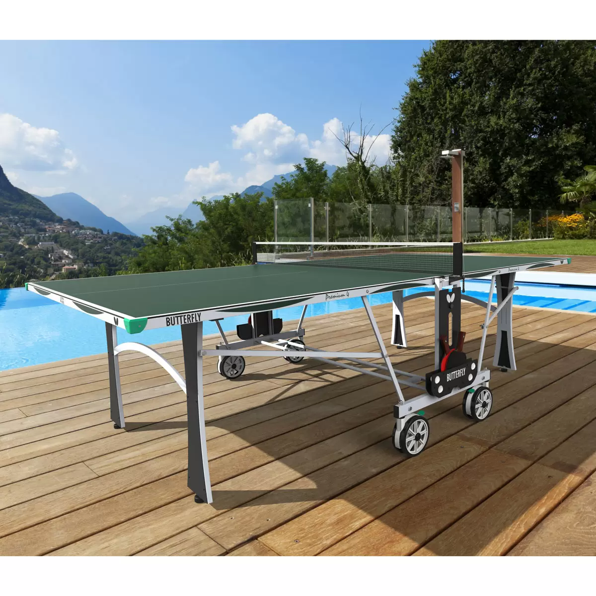Full side view of the blue Butterfly Premium 4 Outdoor Table Tennis Table fully assembled on a backyard stone patio, showing its silver legs and matching green corner bumpers.
