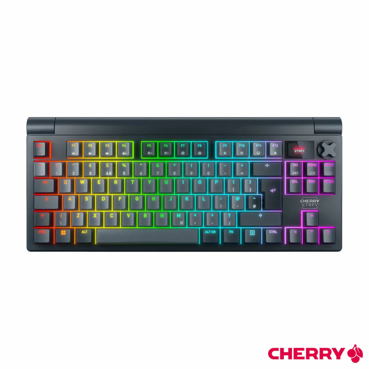 Top-down angled view of the black Cherry XTRFY MX 8.3 TKL wireless mechanical keyboard on a dark desk mat, highlighting the vibrant RGB illumination, crisp PBT keycaps, and active glowing LCD display screen.