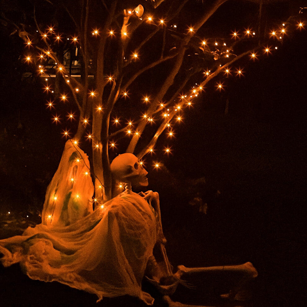 A 20m string of 200 orange LED fairy lights on a black cable glowing across an outdoor haunted house display at night.