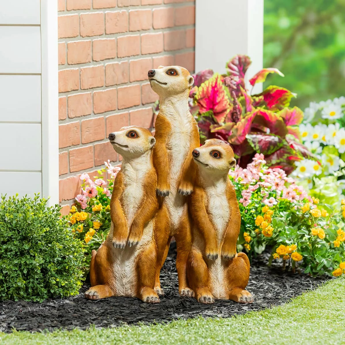 A realistic Evergreen Meerkat Statue standing upright in a "sentry" pose on a stone garden patio.