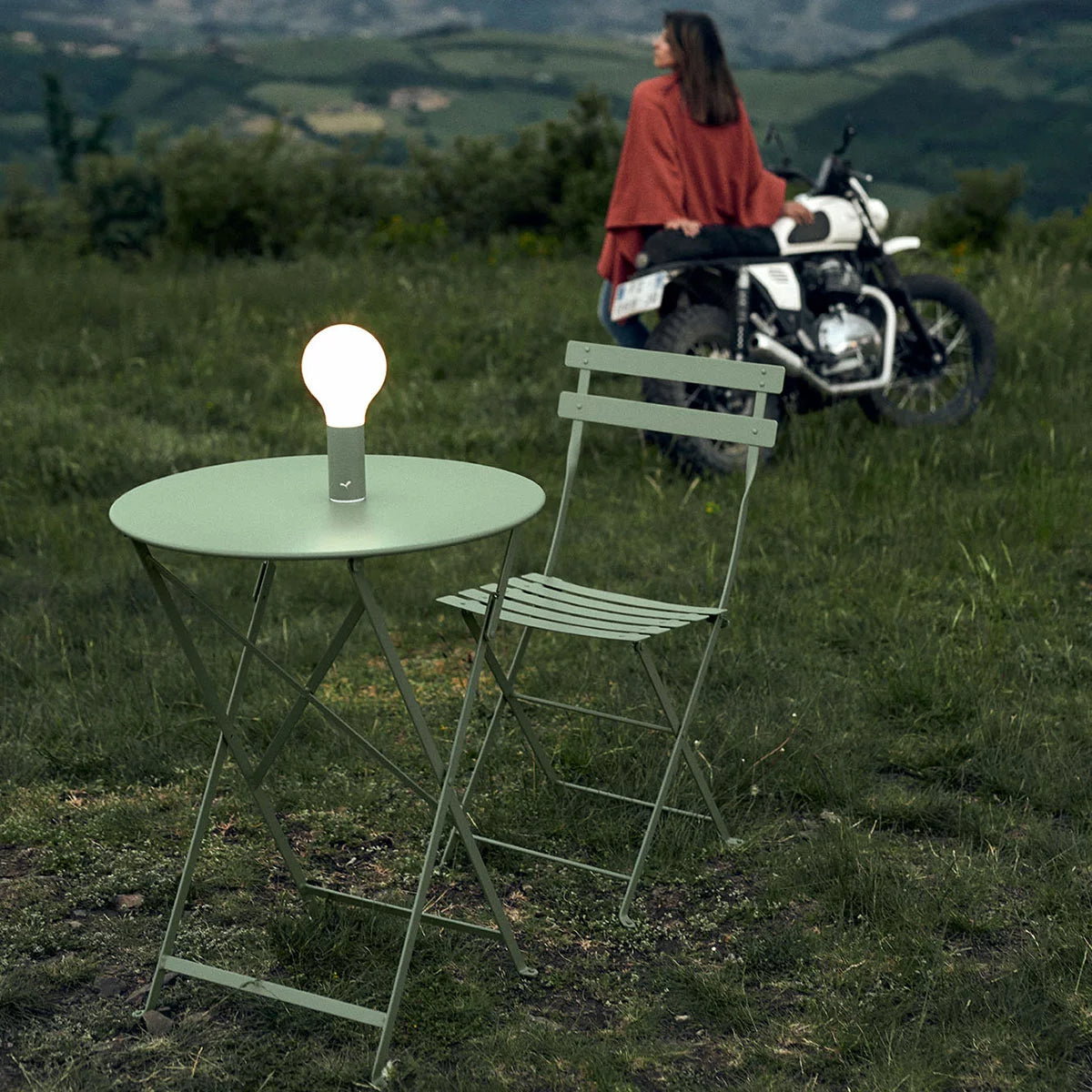Authentic 3-piece Fermob Bistro set in green, styled on a paved patio with vibrant garden plants.