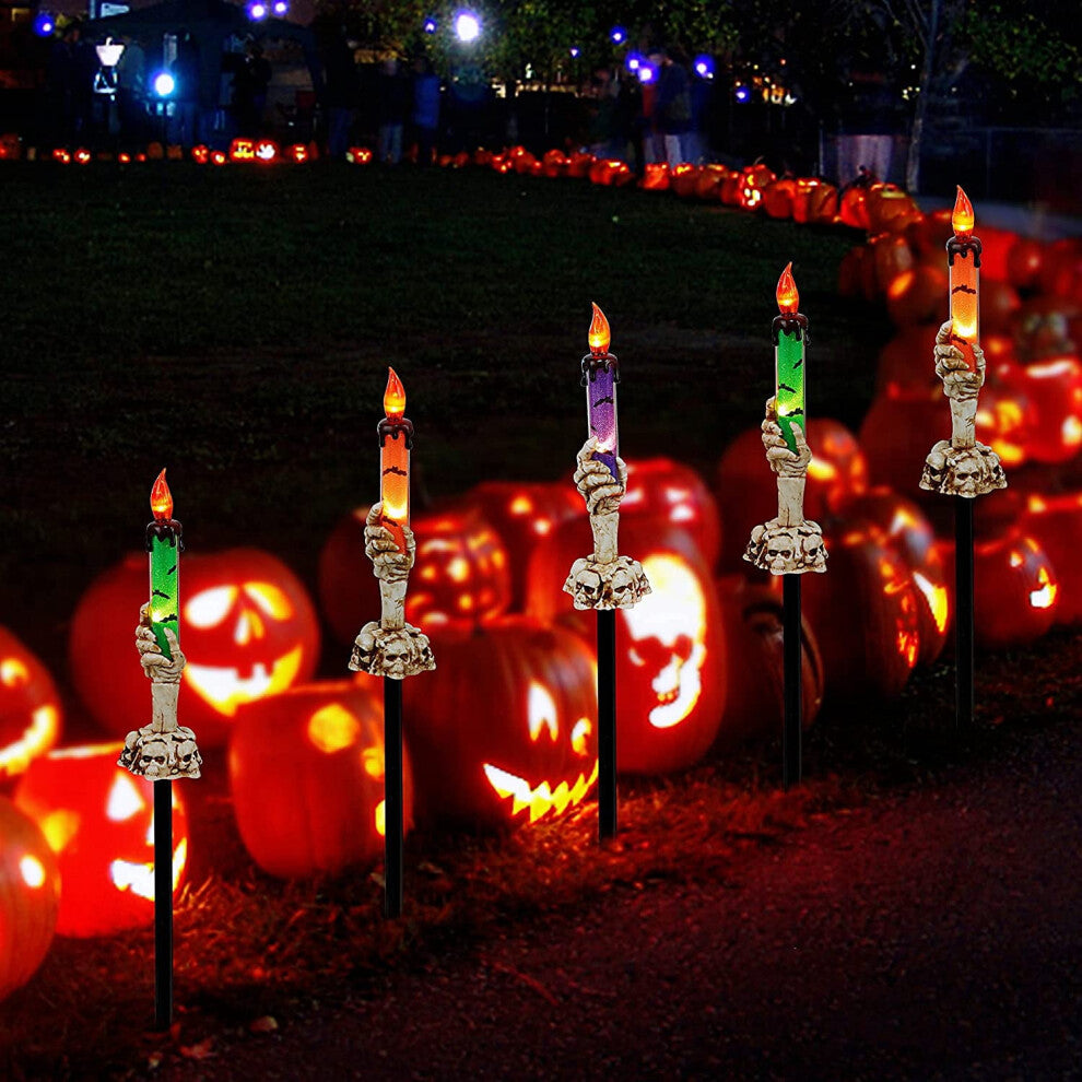 A 5-pack of Halloween lighted skeleton hand candle stakes glowing with warm white LEDs along a spooky outdoor garden lawn