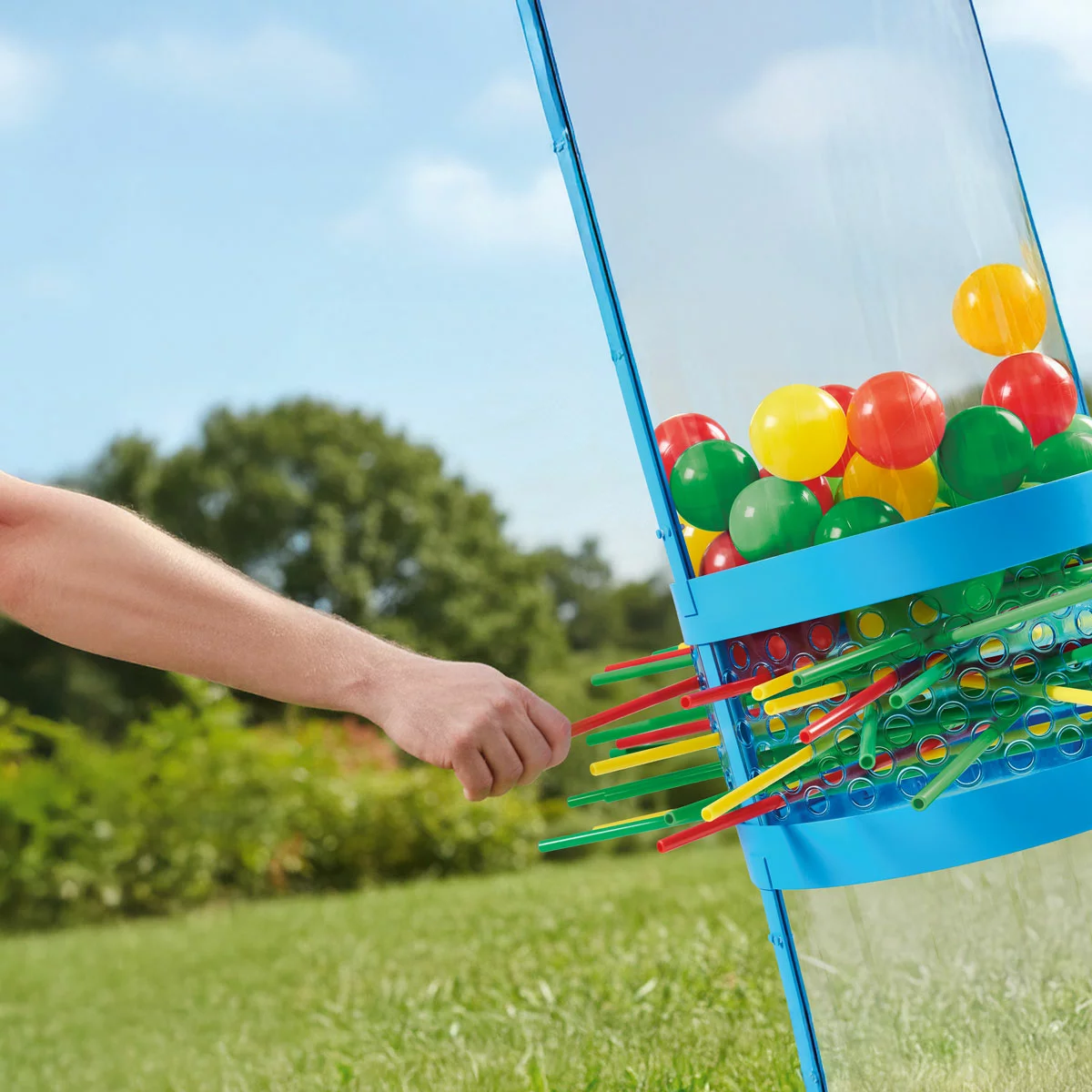 Hasbro Giant KerPlunk Game blue plastic tower standing 91cm tall on an outdoor green lawn with bright multicoloured sticks inserted through the frame holding large balls in place.