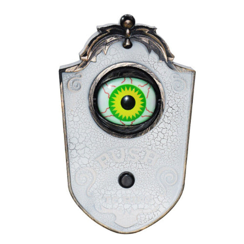 Front view of a black animated haunted eyeball doorbell featuring a scratched bronze texture and a glowing green iris opening on a wooden door frame.