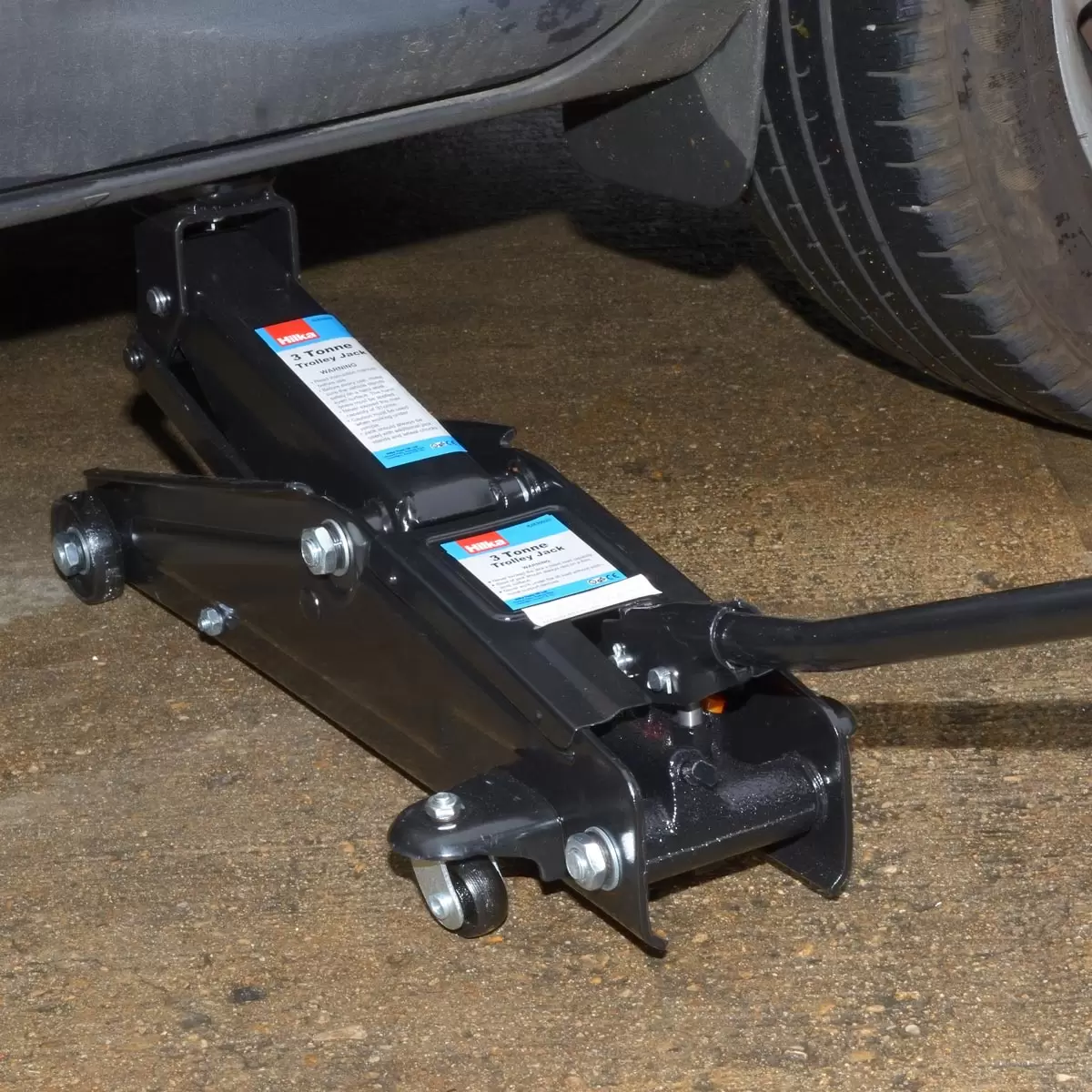Heavy-duty red steel Hilka 3 Tonne Trolley Jack positioned underneath a black 4x4 SUV chassis on a clean concrete garage floor.