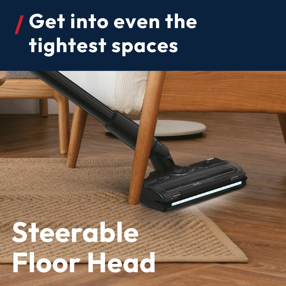 Dark red and grey Hoover HF4 cordless stick vacuum cleaner HF410H standing upright on a wooden floor with its LED headlights illuminating dust under a sofa.