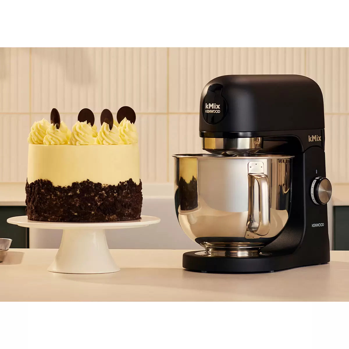 Front profile view of the Kenwood kMix KMX751ABK stand mixer in a matte black finish with its 5-litre stainless steel bowl and K-Beater attachment set up on a kitchen countertop.