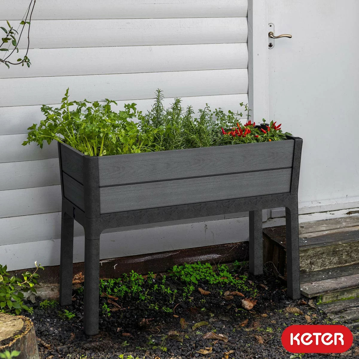 Keter Cortina 1.1m raised garden bed in grey wood-look finish with a water level indicator and thriving green plants.