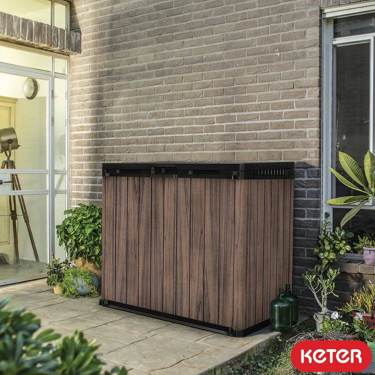 Keter Rosewood 1150L horizontal storage shed with open front doors, sitting neatly against a garden wall, ideal for bin storage.