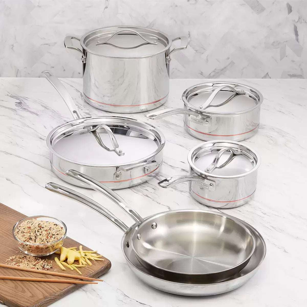 Kirkland Signature 10-piece stainless steel cookware set with copper core layers displayed on a modern kitchen countertop showing saucepans, stockpot, and skillets.