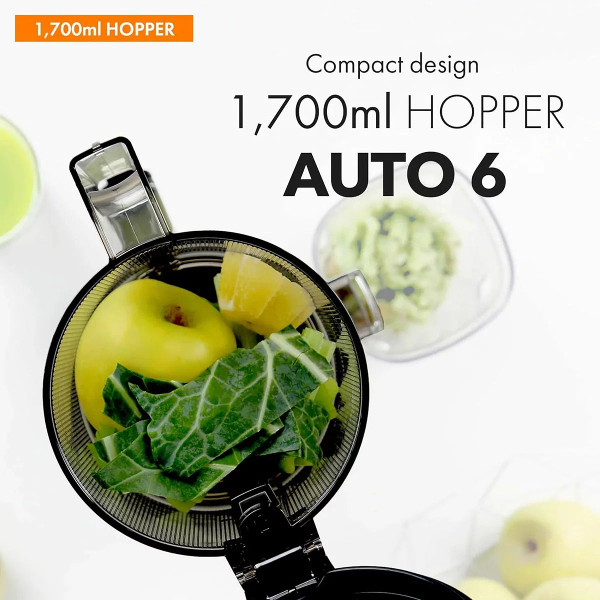 The sleek Kuvings AUTO6 juicer in a modern kitchen setting, showing the large 1.7L auto-hopper filled with fresh apples and citrus, with juice and pulp containers positioned below.