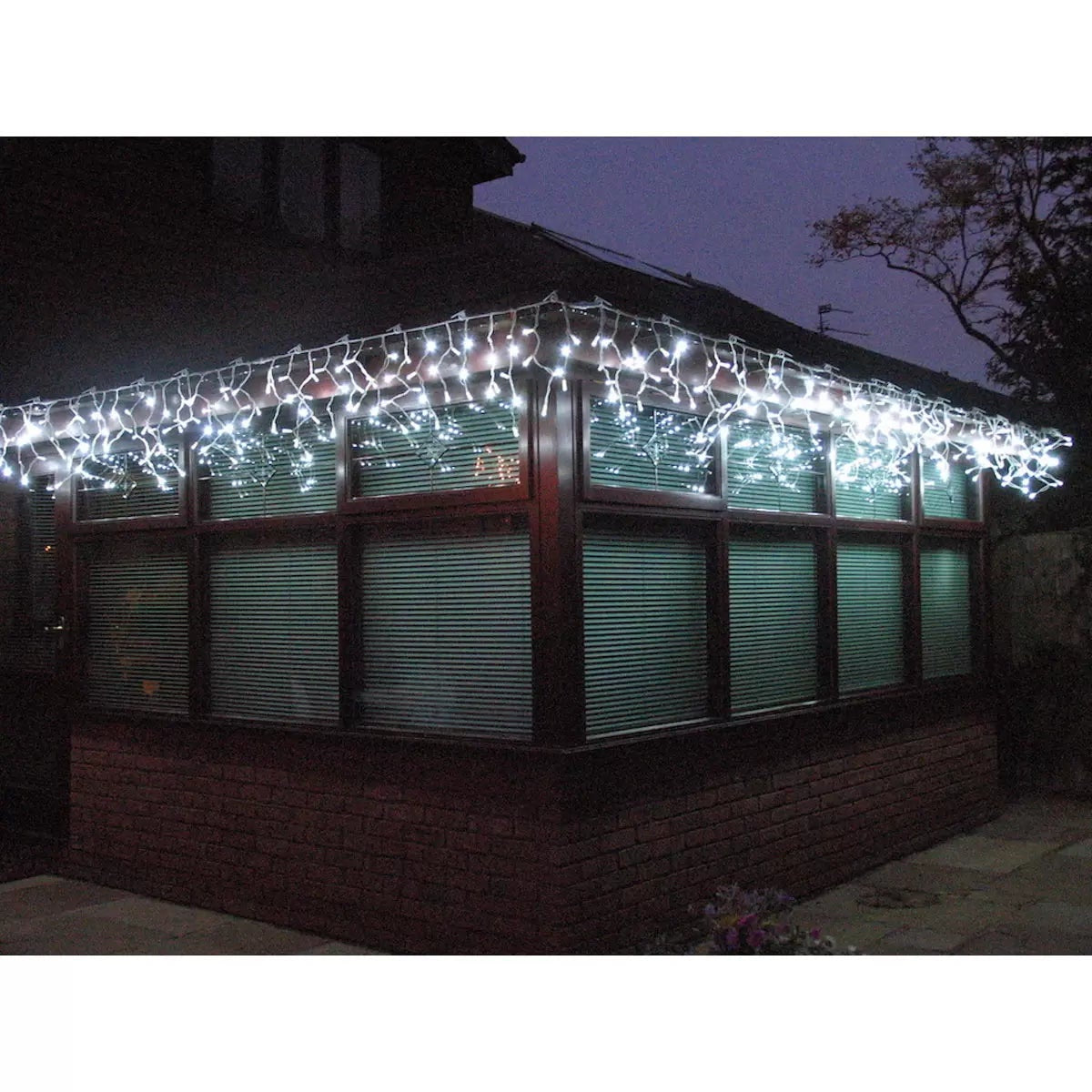 Front view of ice white 152 LED outdoor icicle lights with white cable hanging from a home's roofline at night.