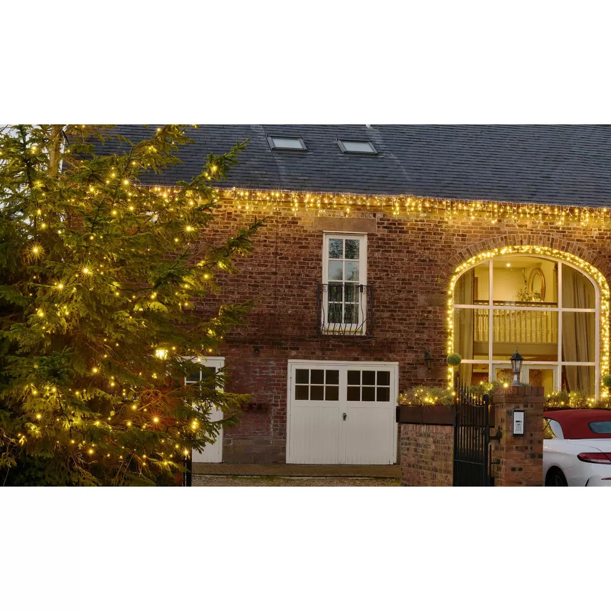 Close up view of warm white LED icicle lights on a white cable hanging along the dark exterior roofline of a modern house at twilight.
