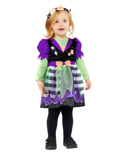 Front view of a toddler girl wearing a purple, green, and orange Little Miss Frankie Frankenstein dress with a matching bow headband in a studio setup.