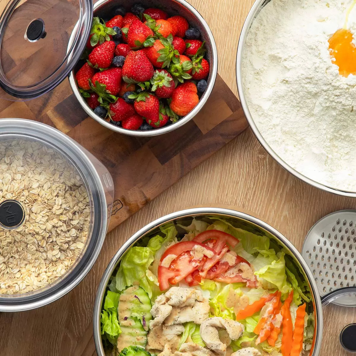Full 11-piece MIU stainless steel mixing bowl set with graters and lids arranged on a kitchen counter.