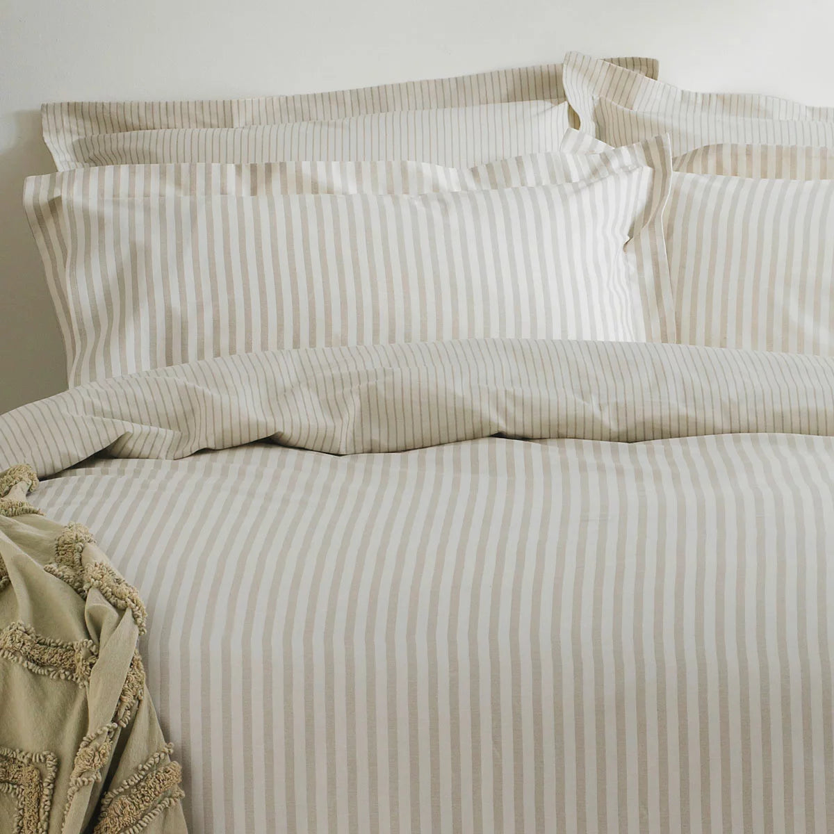 A single bed styled with the Yard Hebden cotton natural stripe duvet cover set, showcasing the soft cream and sand-colored patterns in a bright, modern minimalist room.
