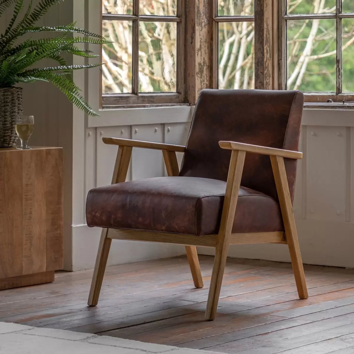 A side angle view of the Gallery Neyland brown leather armchair highlighting its rich top grain upholstery and smooth solid wood frame in a bright room.