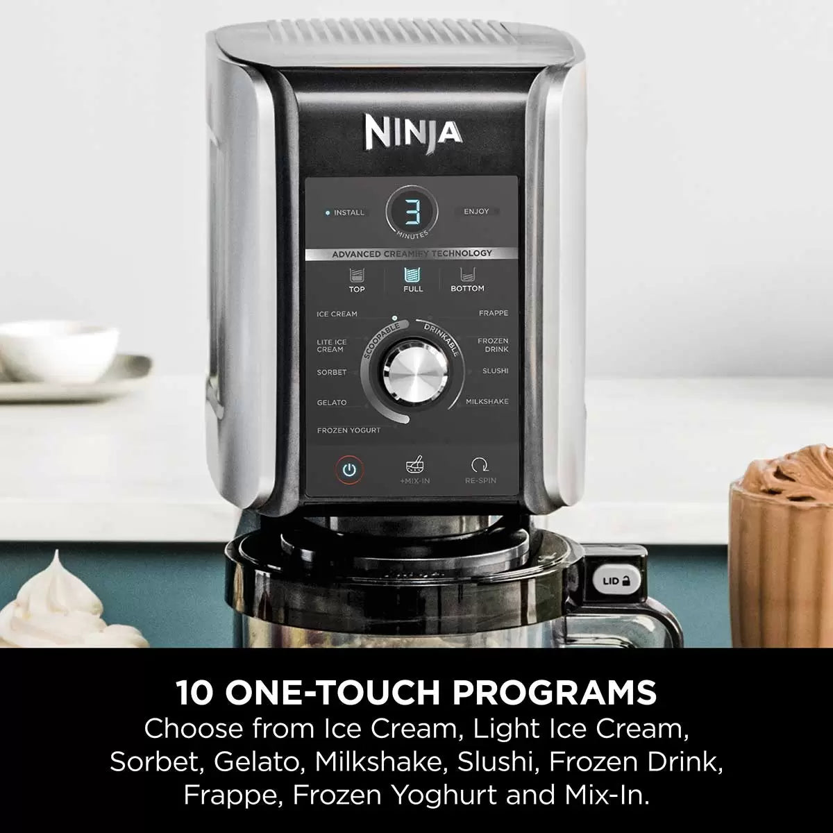 Front view of the matte silver Ninja CREAMi Deluxe NC501UK on a white kitchen counter next to a tub filled with fresh chocolate gelato and berries.