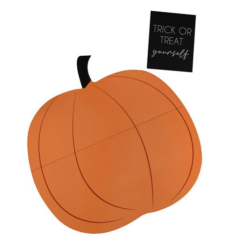 Flat lay view of a pumpkin-shaped wooden grazing board loaded with cheeses, crackers, and fruits on a rustic wooden dining table.