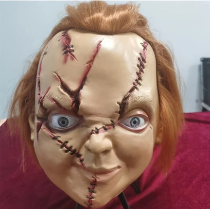 Close-up angle of a realistic Chucky horror latex mask showing detailed stitched facial scars and bright red synthetic hair.