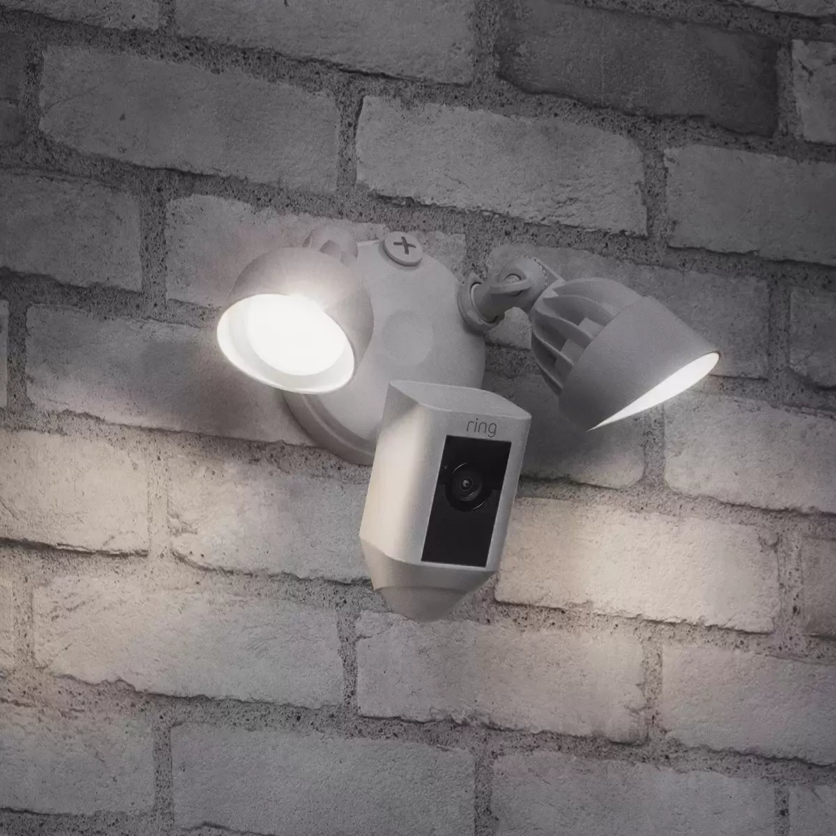 A pair of white Ring Floodlight Cam Plus units mounted on a clean exterior brick wall, showing the dual adjustable LED panels and central camera lens.
