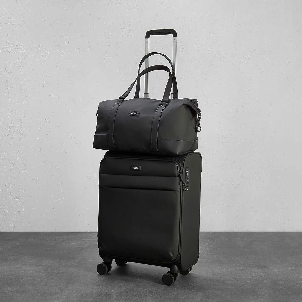 Front perspective view of the navy blue Rock Harper softside cabin suitcase paired with its matching under-seat holdall attached to the telescopic handle in an airport lounge.