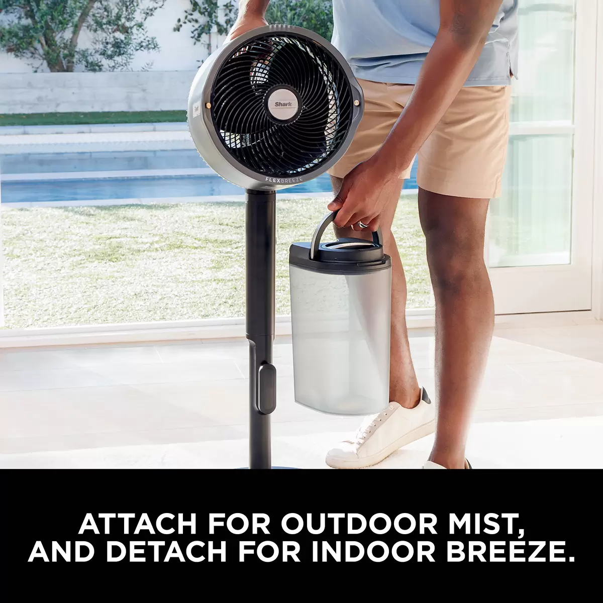 Charcoal grey Shark FlexBreeze Pro Mist fan in pedestal mode spraying a fine cooling mist over a sunny outdoor garden patio setup.