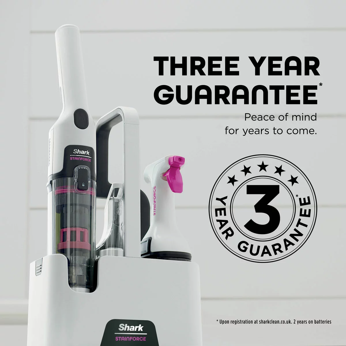 Compact white and grey Shark StainForce cordless spot cleaner HX100UKT standing in its Grab & Go Caddy beside a fabric sofa.