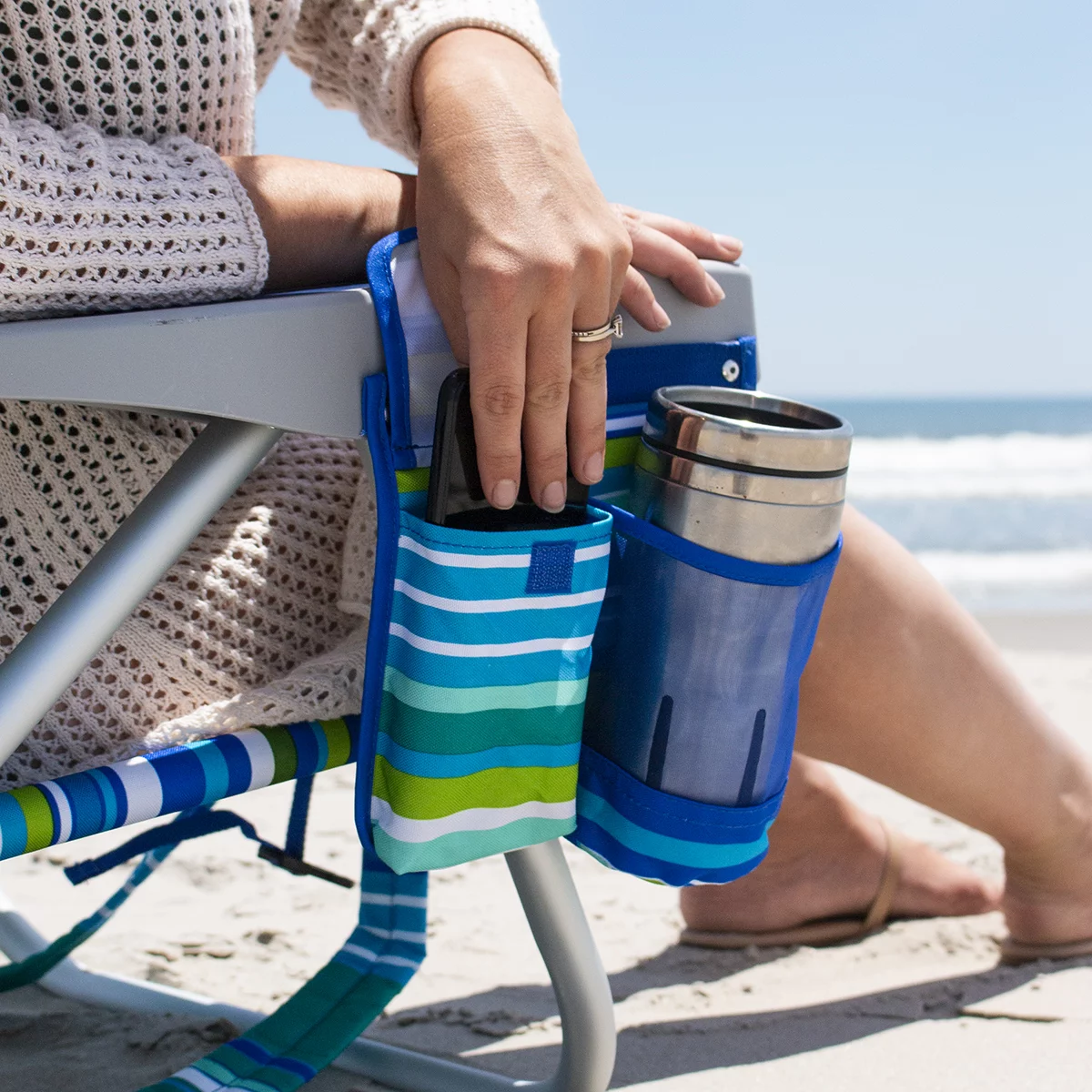 Lightweight blue woven polyester Tommy Bahama backpack beach chair with padded shoulder straps, drink holder, and integrated rear cooler pouch unfolded on a sandy beach.