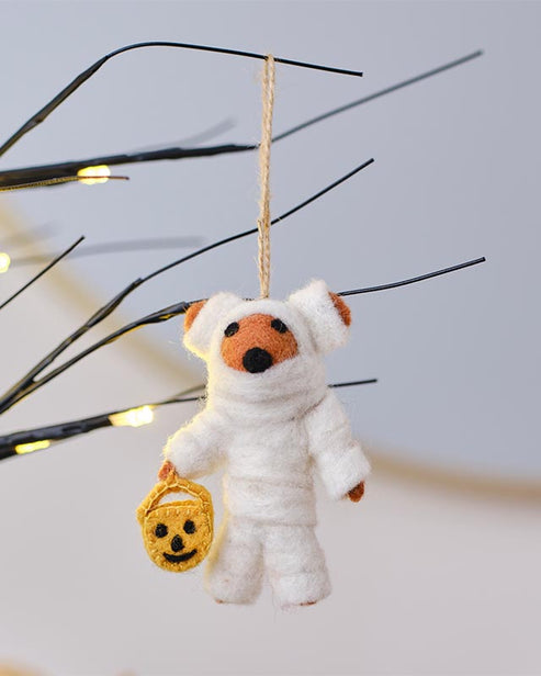 Textured white cloth wrapped mummy tree decoration with dark eye details hanging on a spooky indoor Halloween tree branch.