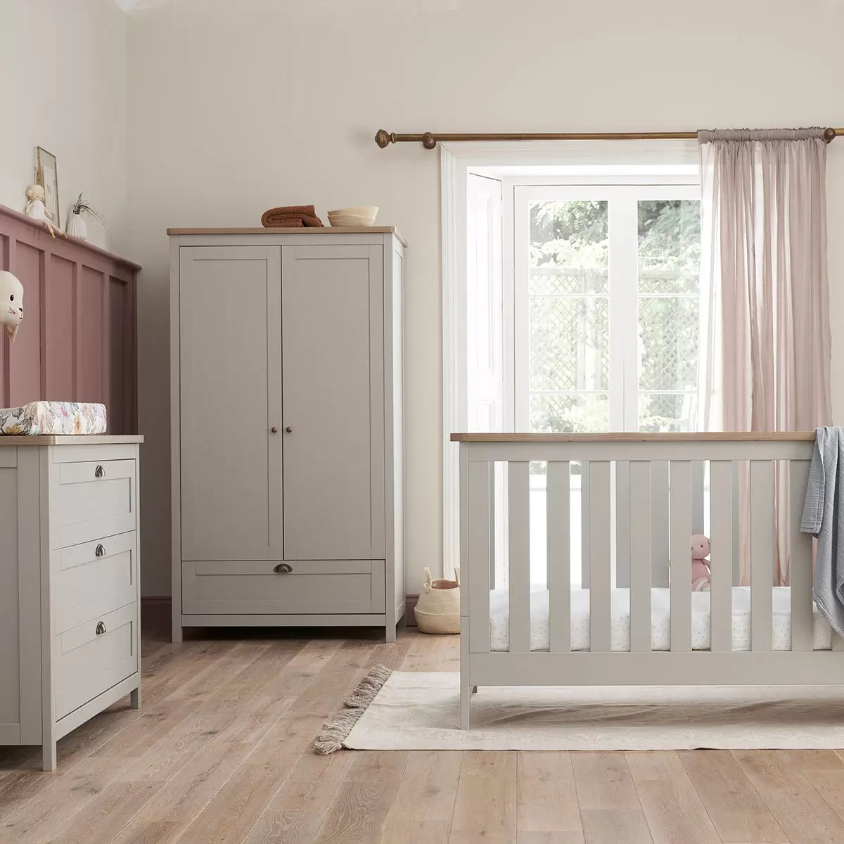 Front view of the Tutti Bambini Verona Wardrobe in soft-touch grey and oak finish with antique brass handles inside a modern nursery.