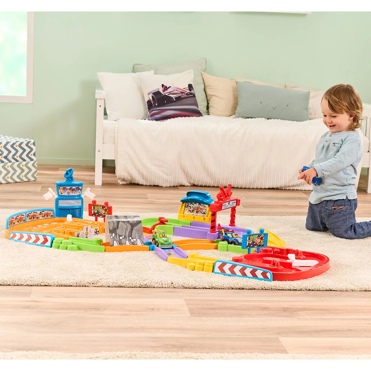 Brightly colored VTech Toot-Toot Drivers Super Circuit RC Raceway plastic track layout featuring a red RC car, motorized racer, tunnel, and remote control on a light wood floor.