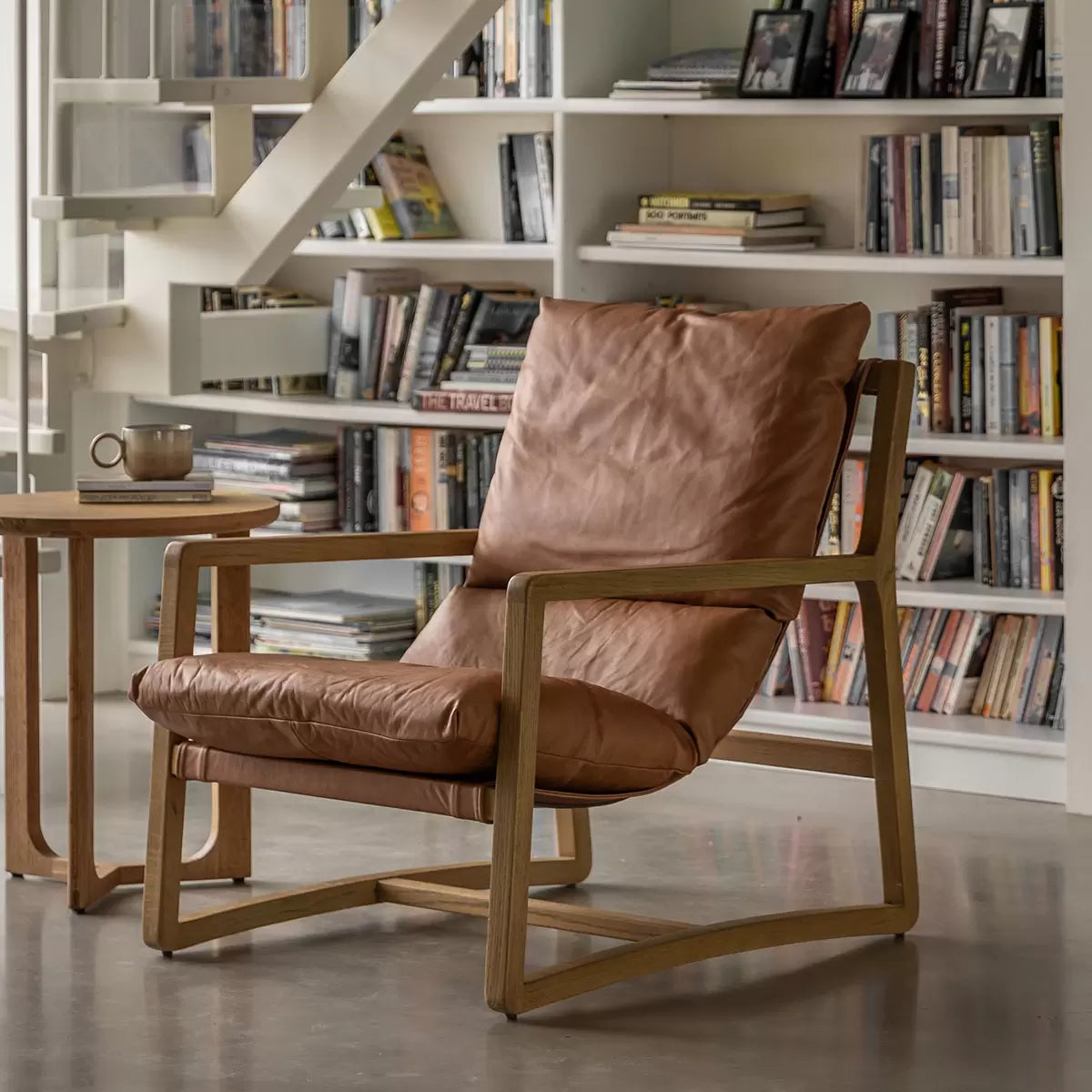 A close-up angled shot of the Gallery Burela Lounge Chair highlighting its vintage brown leather creases, plush seat cushion, and natural grain of the light ash wood legs.