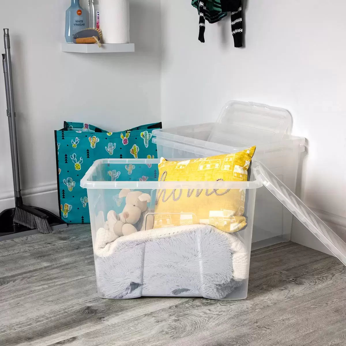 Three stacked Wham 80L crystal clear plastic storage boxes with matching snap-on lids arranged vertically in a bright, organized home utility room setting.