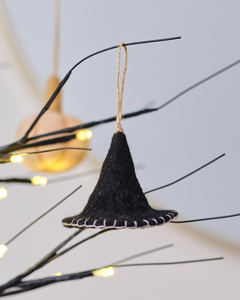 Black velvet witches hat tree decoration featuring a pointed tip and wide brim hanging on a dark evergreen branch.