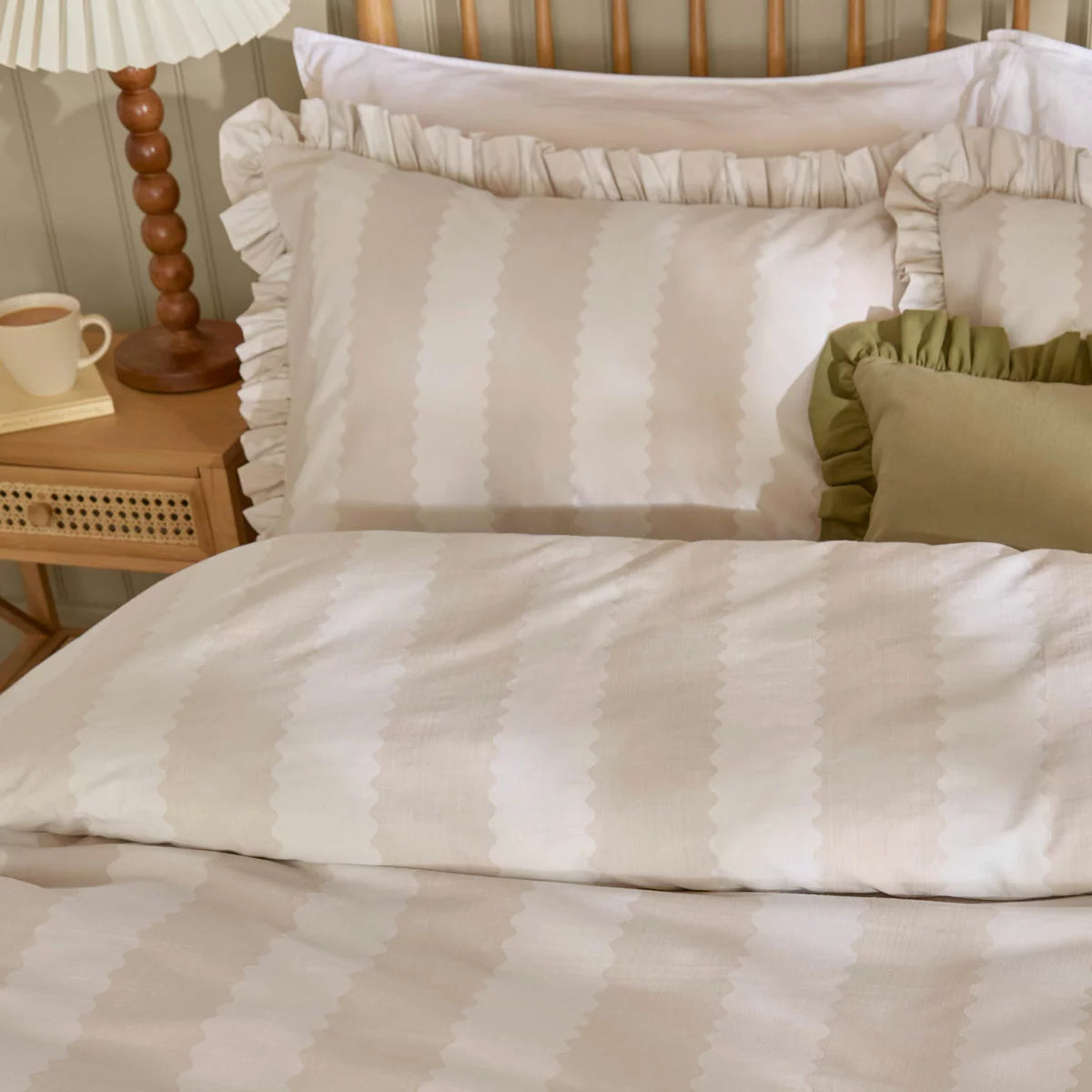 A close-up view of the Wylder Birdie beige stripe duvet cover showing its vintage ruffle trim detail draped over a cozy mattress in a brightly lit bedroom.