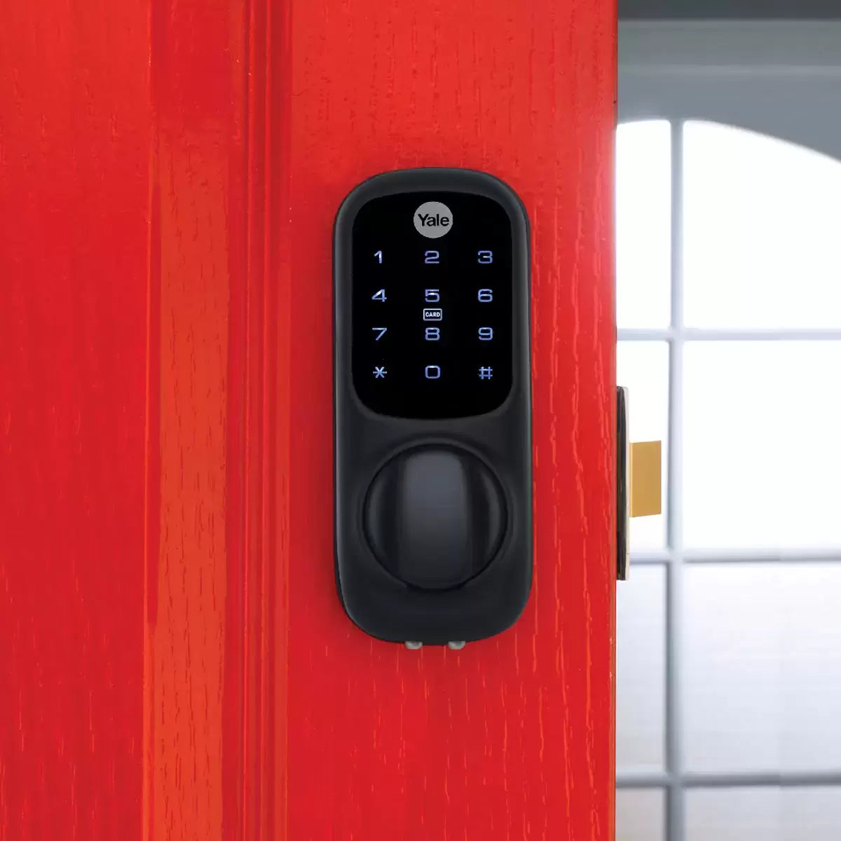 A close-up shot of the matte black Yale Keyless Smart Lock displaying illuminated blue numbers on its digital touch screen, mounted onto a modern dark oak wooden door.