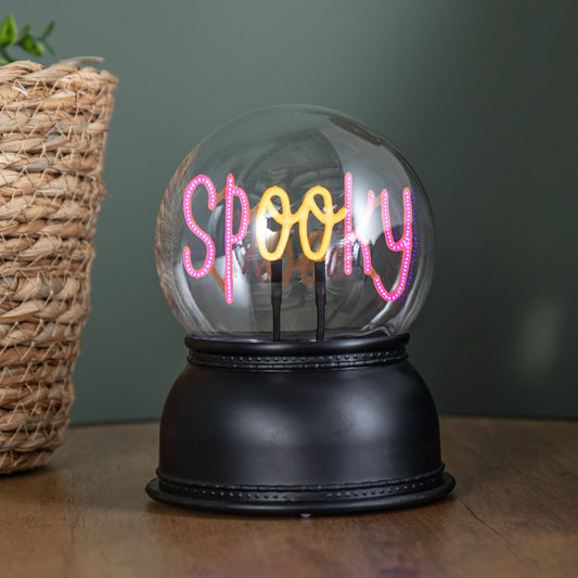 Front view of the 14cm Samuel Alexander spooky Halloween globe illuminating the word SPOOKY with a purple and orange LED light on a wooden table.