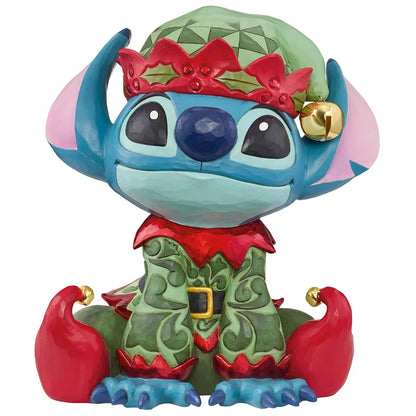 Front angle view of a 14-inch hand-painted Disney Elf Stitch statue by Jim Shore featuring green elf hat, jingle bells, and detailed stone resin folk patterns on a wooden table.