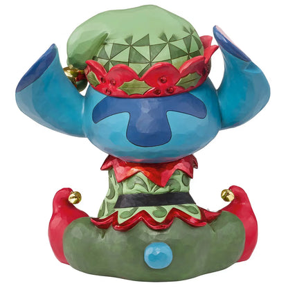 Front angle view of a 14-inch hand-painted Disney Elf Stitch statue by Jim Shore featuring green elf hat, jingle bells, and detailed stone resin folk patterns on a wooden table.