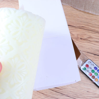 A 15cm white paraffin wax flameless LED candle featuring an intricate hollow flower pattern glowing softly on a decorative table.