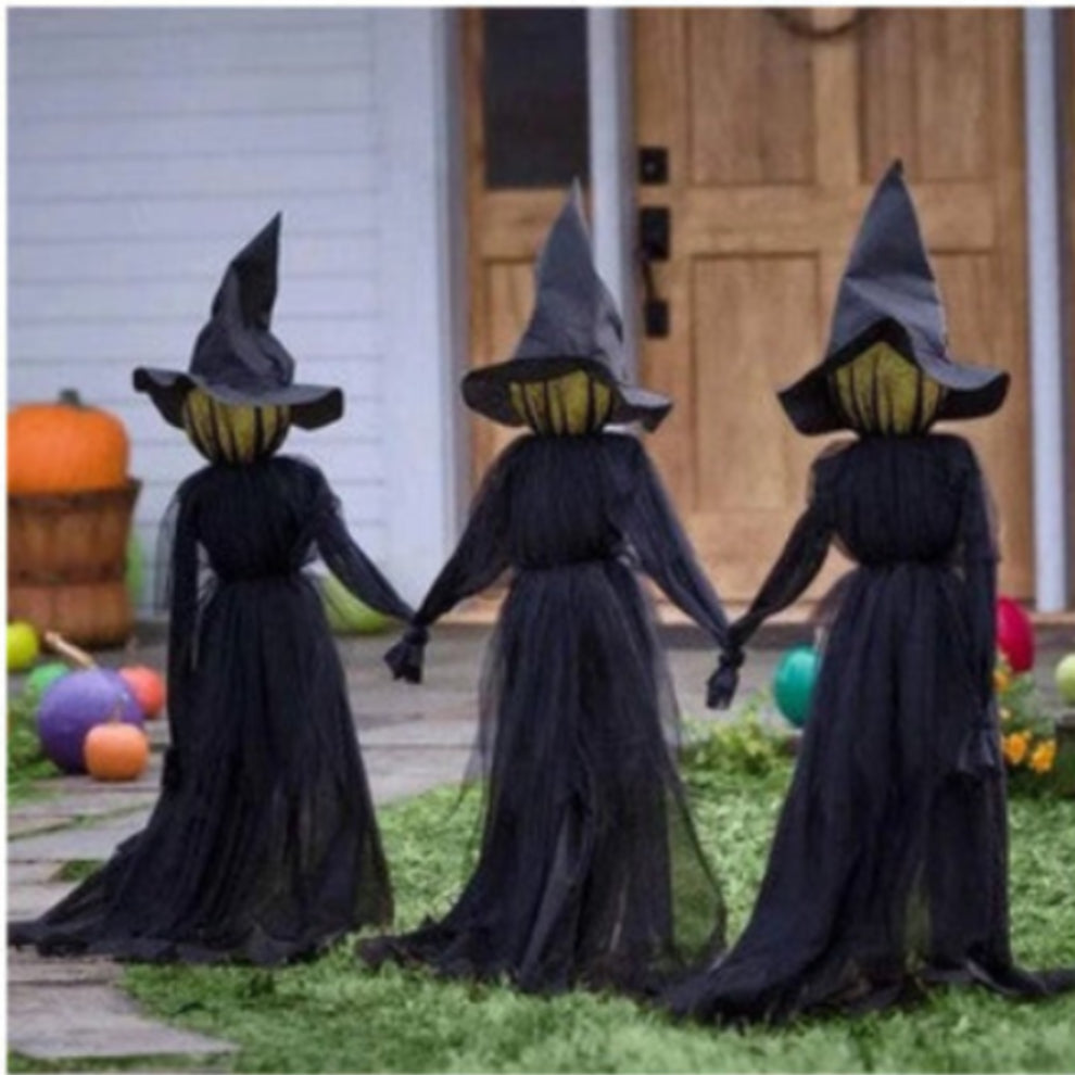 Front view of three 170cm life-size faceless witches in black robes holding hands on a dark lawn with glowing heads flickering in the dark.